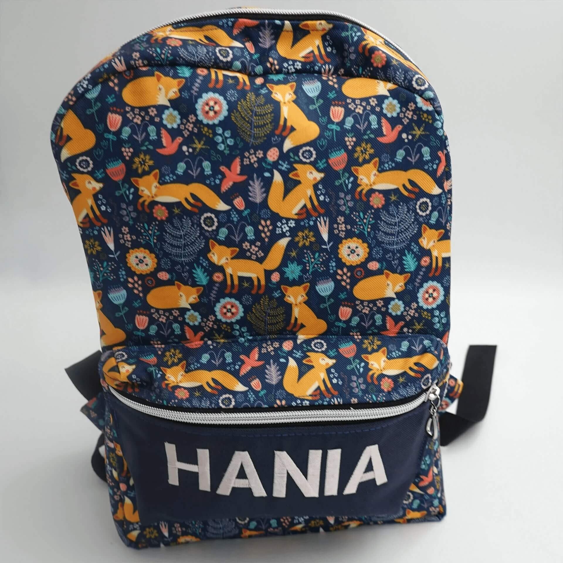 Dziecięcy plecak z motywem lisów i kwiatów na granatowym tle, z imieniem 'HANIA' nadrukowanym na dolnej kieszeni.