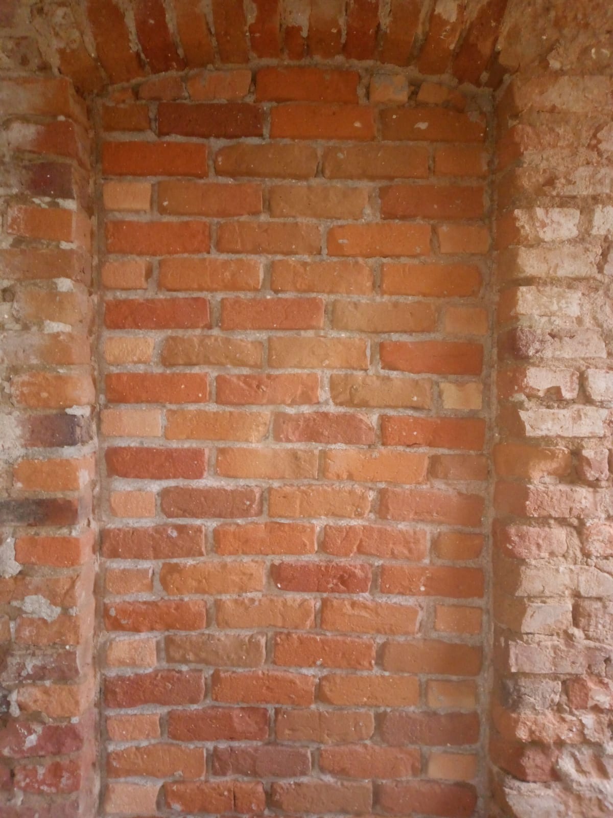 Ceglana ściana z wnęką w kształcie łuku, po piaskowaniu widoczne różnice w kolorze cegieł.