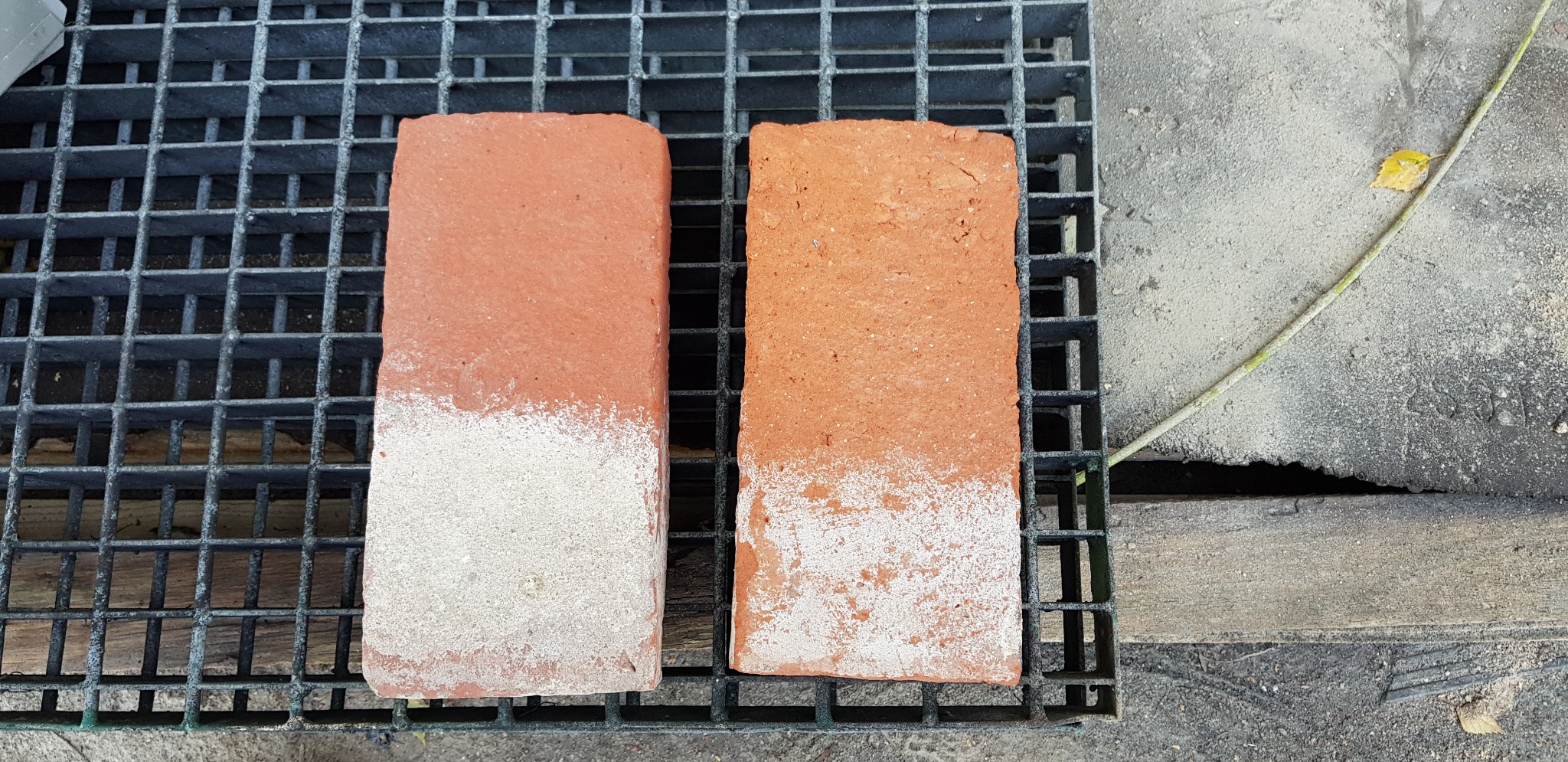 Dwie cegły po częściowym oczyszczeniu, leżące na metalowej kratce, pokazujące różnicę w wyglądzie przed i po procesie czyszczenia.