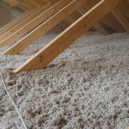 Izobud - Poddasze z drewnianą konstrukcją krokwi i warstwą izolacji z wełny celulozowej, widoczny kabel elektryczny.