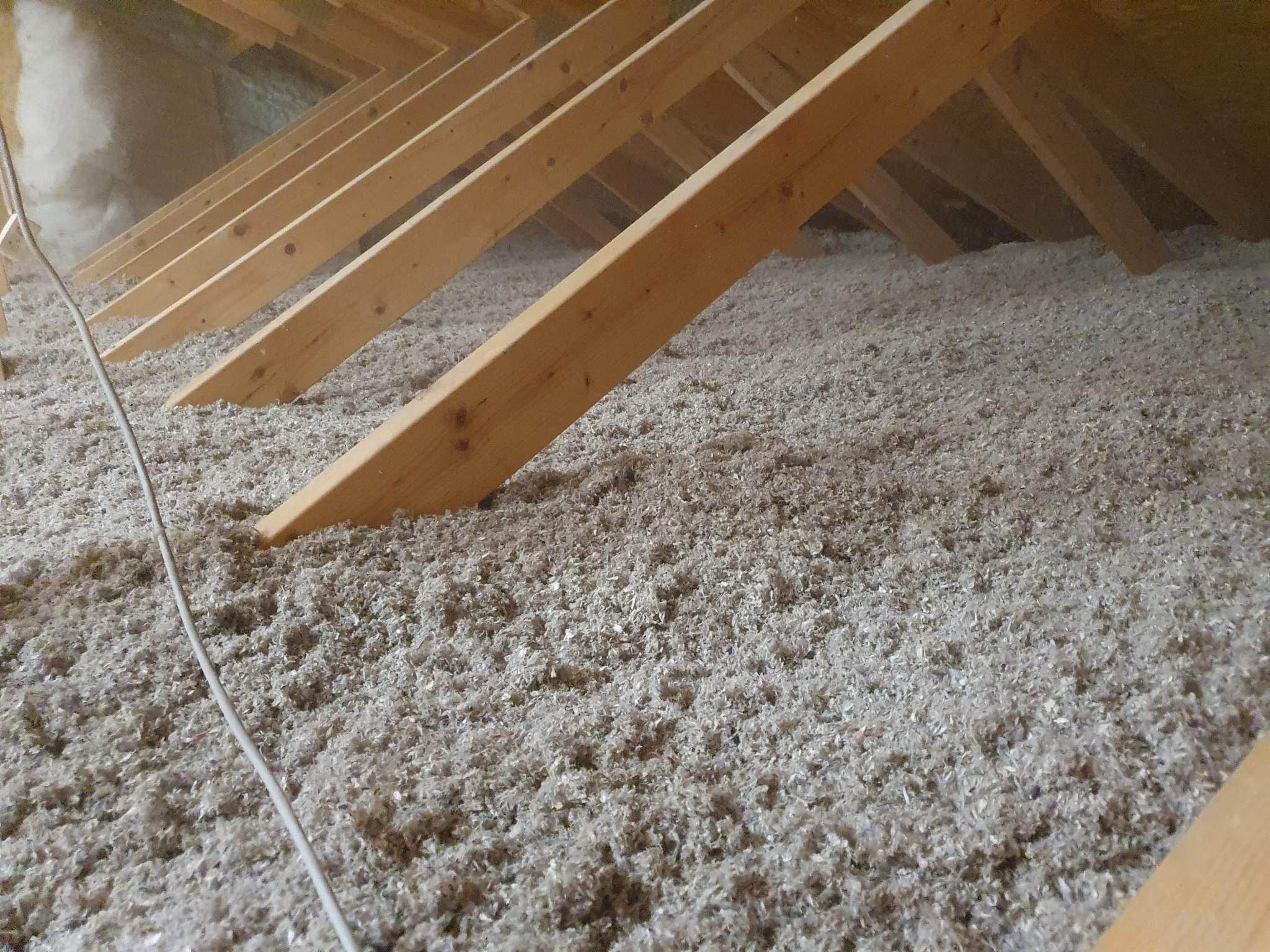 Poddasze z drewnianą konstrukcją krokwi i warstwą izolacji z wełny celulozowej, widoczny kabel elektryczny.