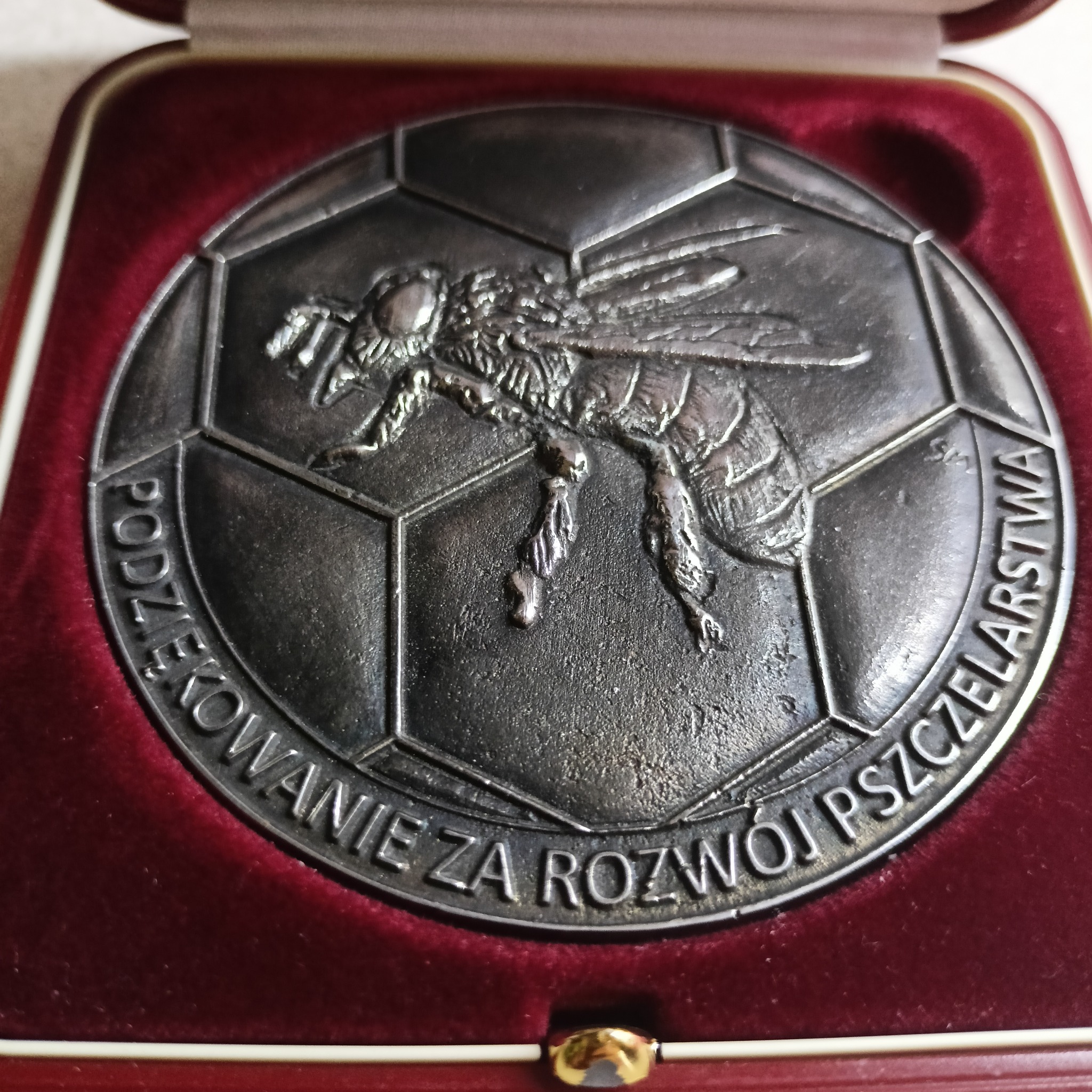 Srebrny medal z wizerunkiem pszczoły i napisem 'Podziękowanie za rozwój pszczelarstwa' w czerwonym, aksamitnym etui.