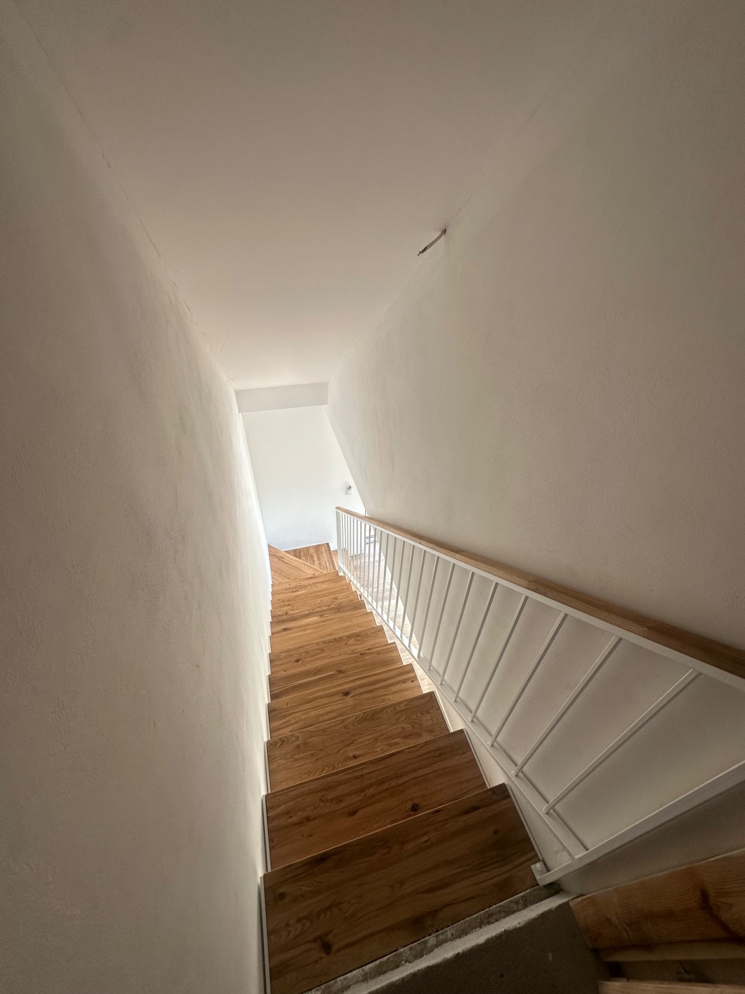 Wnętrze domu z drewnianymi schodami z białymi metalowymi barierkami widzianymi z góry.