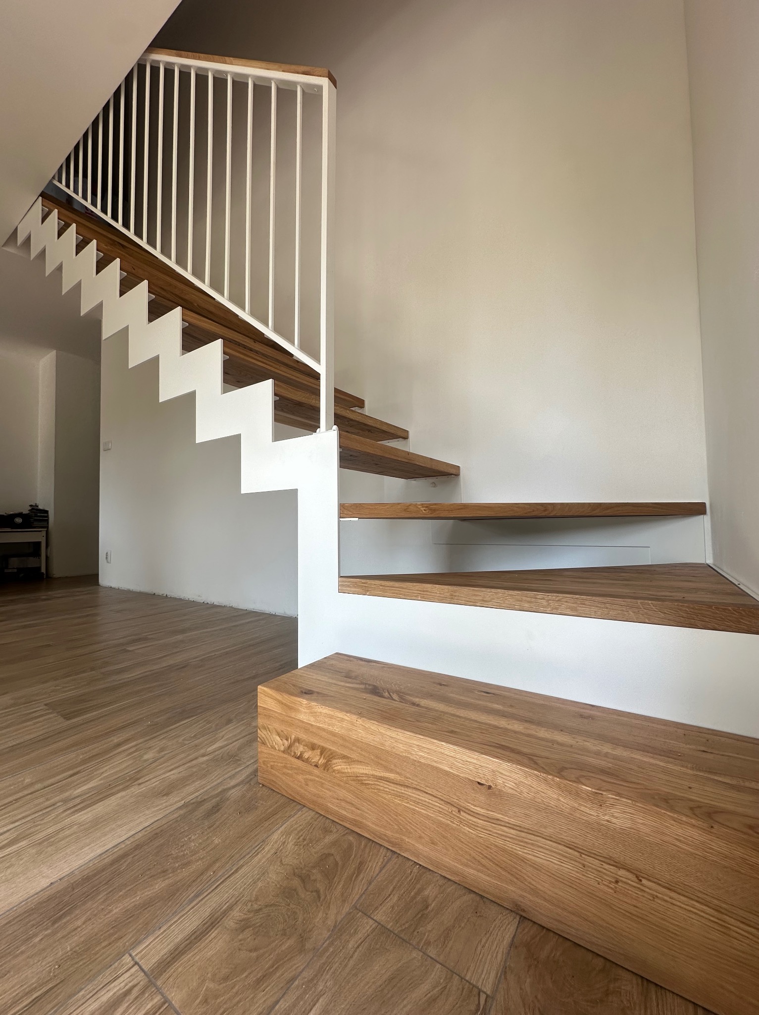 Nowoczesne schody z drewnianymi stopniami i białą metalową konstrukcją oraz minimalistyczną balustradą, widok z dołu.