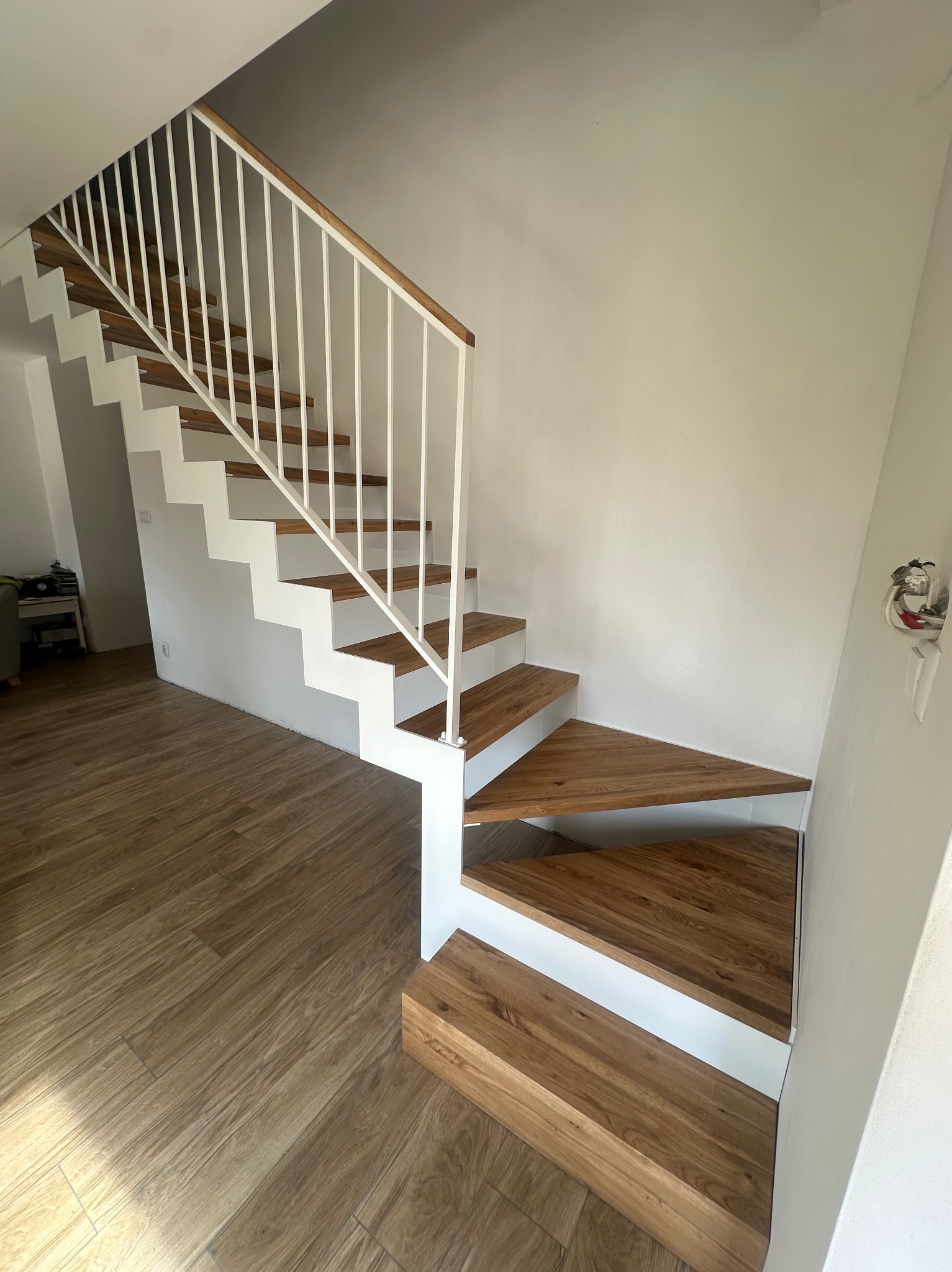 Nowoczesne schody z drewnianymi stopniami i białą metalową balustradą w jasnym wnętrzu, widok z dołu.