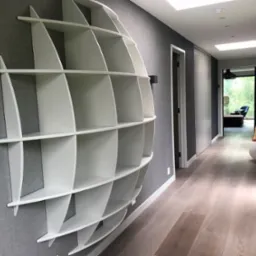 Biała, półokrągła, designerska półka na szarej ścianie w korytarzu z drewnianą podłogą i oknami dachowymi.