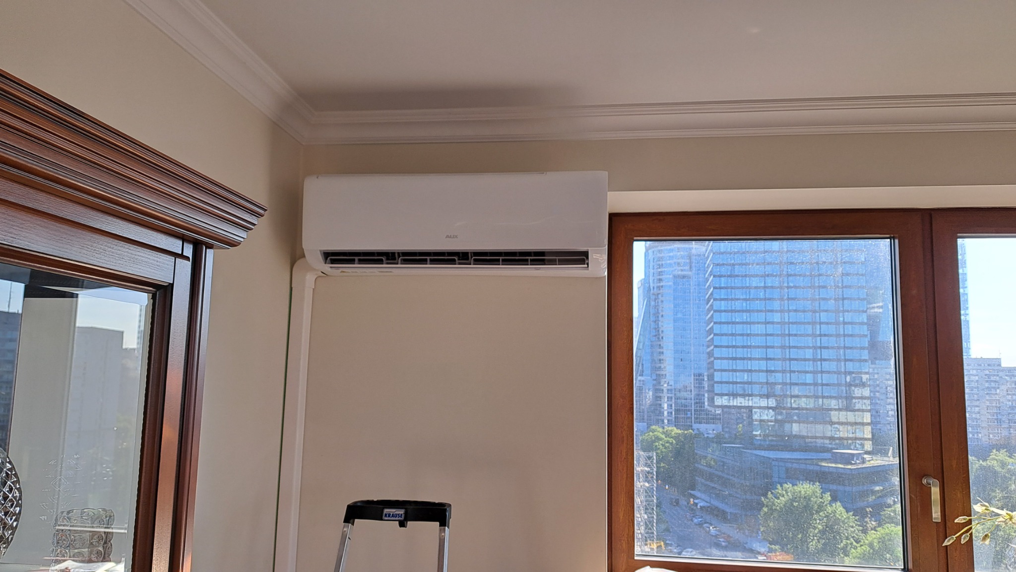 Zamontowana klimatyzacja AUX w jasnym wnętrzu, widok na miasto przez okno, drabina Krause gotowa do użycia.