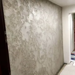 Ściana z dekoracyjną, szarą strukturą w Mysłowicach, imitującą kamień, widoczna z boku, z fragmentem futryny drzwi po lewej stronie.