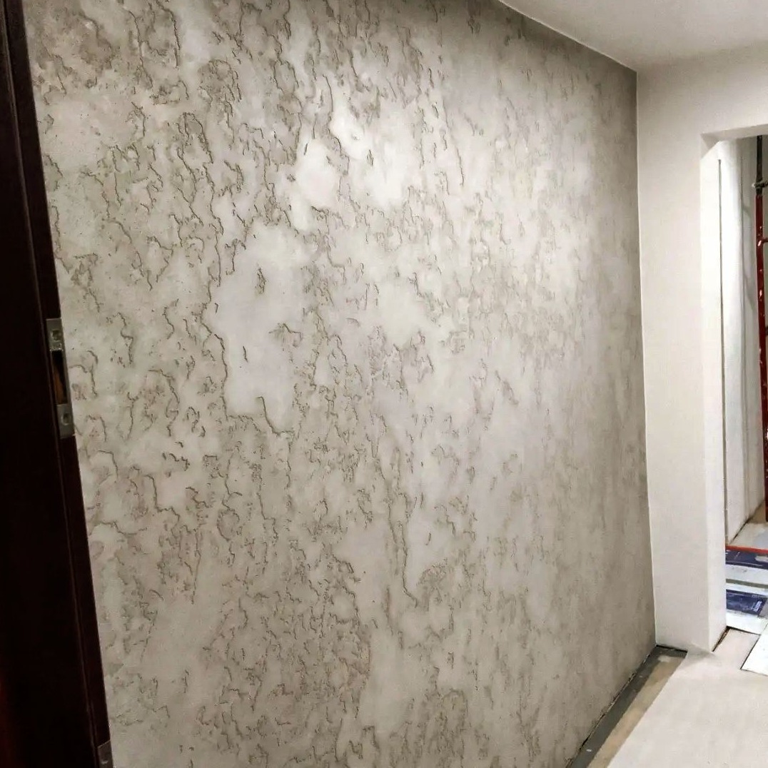 Ściana z dekoracyjną, szarą strukturą w Mysłowicach, imitującą kamień, widoczna z boku, z fragmentem futryny drzwi po lewej stronie.