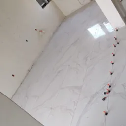 Świeżo ułożone, białe płytki podłogowe z marmurowym wzorem, z użyciem poziomujących klipsów i klinów, widoczne przygotowane ściany i fragment kolumny.