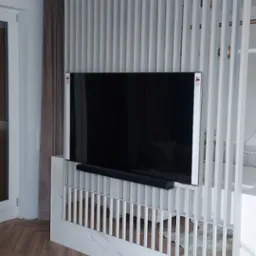 Nowoczesna aranżacja salonu z telewizorem na ścianie z białych, pionowych listew, marmurowy cokół, parkiet w jodełkę i złoty stolik kawowy