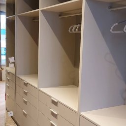 Meble Wirkos - Wnętrze szafy z szufladami i półkami w odcieniach beżu i szarości, widoczne drążki na wieszaki i puste wieszaki. Lustrzane drzwi szafy po lewej stronie.