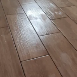 Ułożone, brązowe panele podłogowe imitujące drewno, widoczne fugi i faktura drewna, przy ścianie widoczne ślady po pracach wykończeniowych.