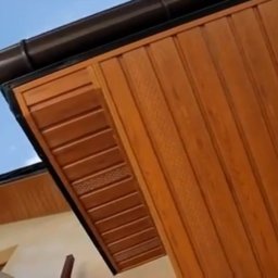 DMX USŁUGI TRANSPORTOWO - BUDOWLANE Jarosław Wolski - Drewniana podbitka dachowa w odcieniach brązu, widoczna z dołu pod kątem. Na górze brązowa rynna, w tle fragment błękitnego nieba z chmurami.