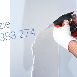 DMX USŁUGI TRANSPORTOWO - BUDOWLANE Jarosław Wolski - Nakładanie gładzi na ścianę za pomocą szpachelki. Widoczne ręce w rękawicach i fragment ściany z nałożoną gładzią. Na ścianie numer telefonu do wykonawcy.