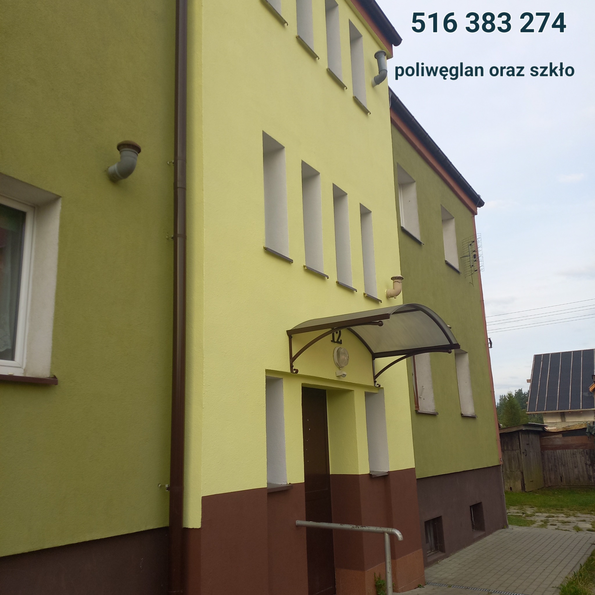 Odnowiona elewacja dwukondygnacyjnego budynku w odcieniach zieleni i brązu, z numerem 12 nad wejściem i widoczną instalacją odgromową na dachu sąsiedniego budynku.