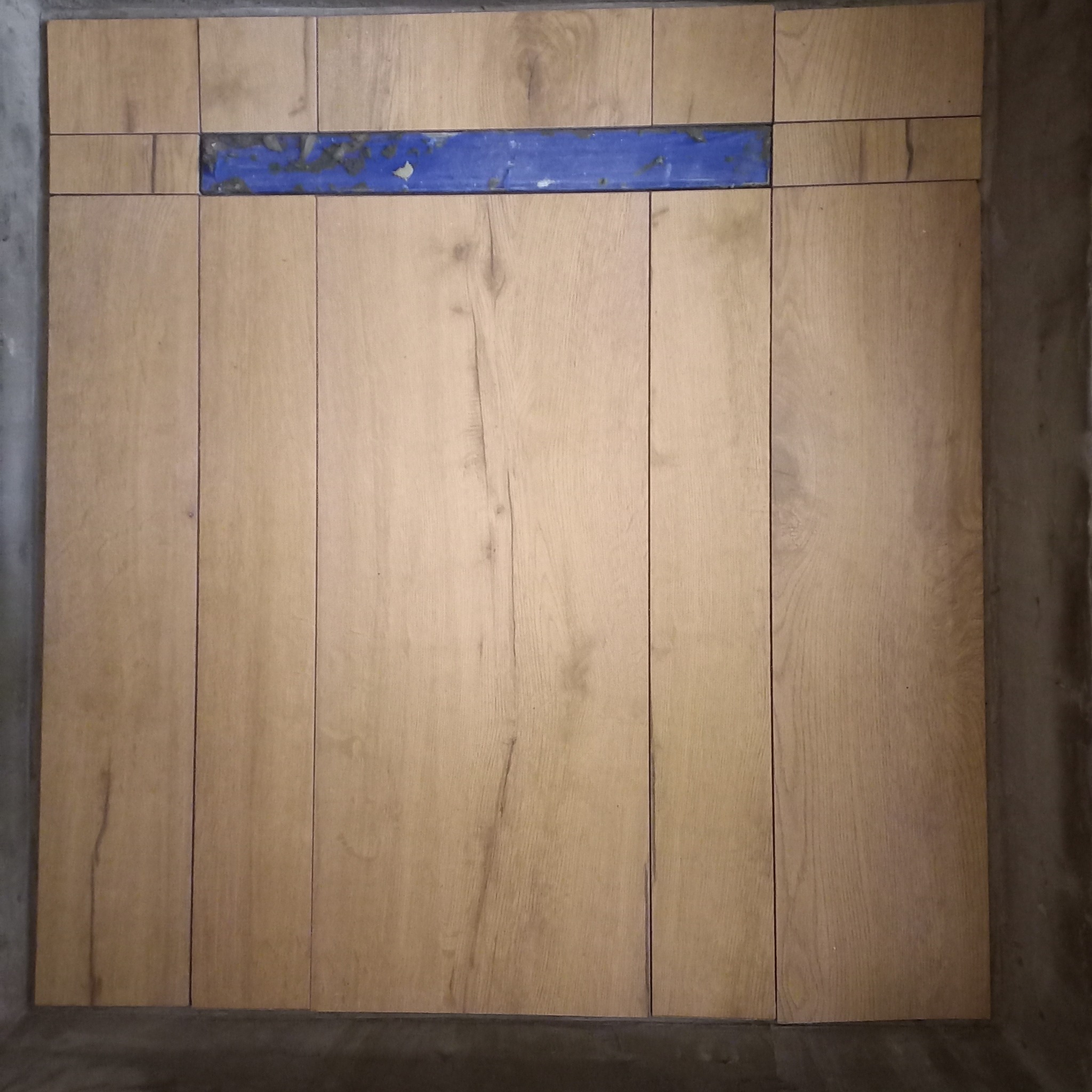 Układanie paneli ściennych z drewnopodobnym wzorem, z widocznym niebieskim elementem montażowym. Surowe, betonowe wykończenie ścian w tle.