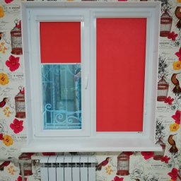 Oleksandr Kozachenko - Białe okno PCV z dwoma skrzydłami, jedno z częściowo opuszczoną czerwoną roletą, drugie z widoczną kratą w oknie, na tle kwiecistej tapety z motywem klatek dla ptaków.