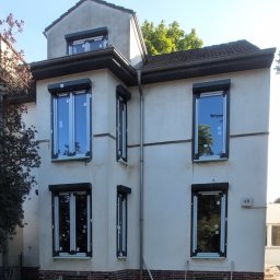 Oleksandr Kozachenko - Dwupiętrowy dom z nowymi oknami i roletami zewnętrznymi, w trakcie wykończenia elewacji, widoczne gruz i materiały budowlane.