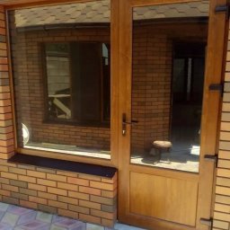 Oleksandr Kozachenko - Brązowe drzwi wejściowe z szybą i oknem bocznym, osadzone w murze z cegły klinkierowej, widok z zewnątrz.