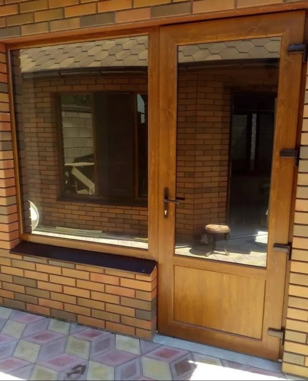 Brązowe drzwi wejściowe z szybą i oknem bocznym, osadzone w murze z cegły klinkierowej, widok z zewnątrz.