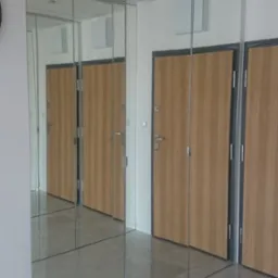 Wysoka szafa z lustrzanymi drzwiami przesuwnymi, integrująca się z wystrojem przedpokoju, odbijająca drzwi wejściowe i światło, tworząc efekt przestronności.