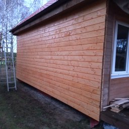 Adam kawa Profix - Świeżo wybudowana altana z jasnego drewna, widoczna drabina oparta o ścianę, podłoże częściowo wyłożone kamieniami.