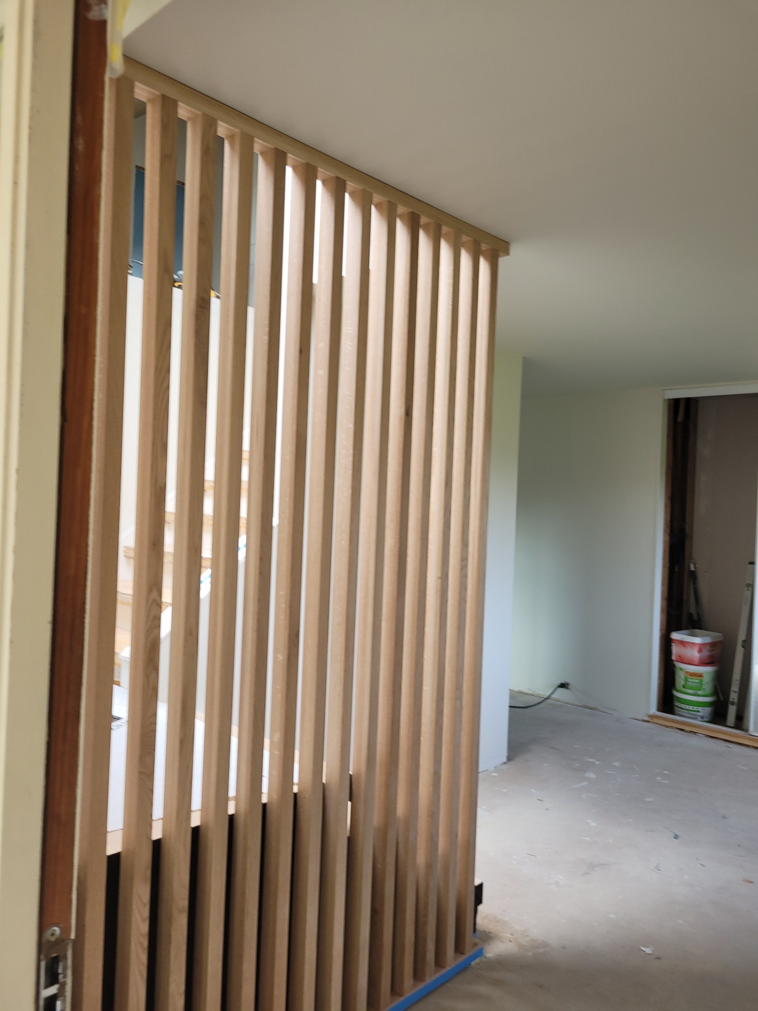 Drewniana ażurowa ścianka działowa z pionowych listew oddzielająca przestrzeń wewnątrz remontowanego mieszkania, widoczne schody w tle.