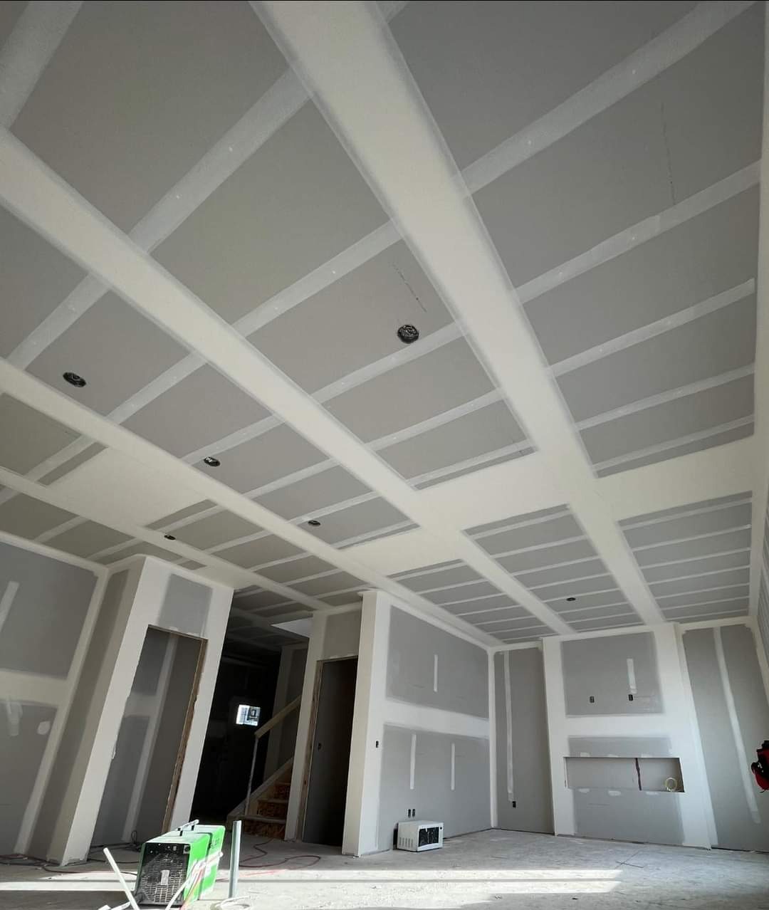 Sufit i ściany w trakcie montażu płyt kartonowo-gipsowych, widoczne profile nośne i otwory na oświetlenie, na podłodze leży sprzęt budowlany.