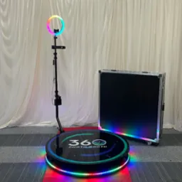 Profesjonalna, rozłożona fotobudka 360 stopni z podświetleniem LED w kolorach tęczy, gotowa do użycia, obok znajduje się czarny case transportowy na kółkach.