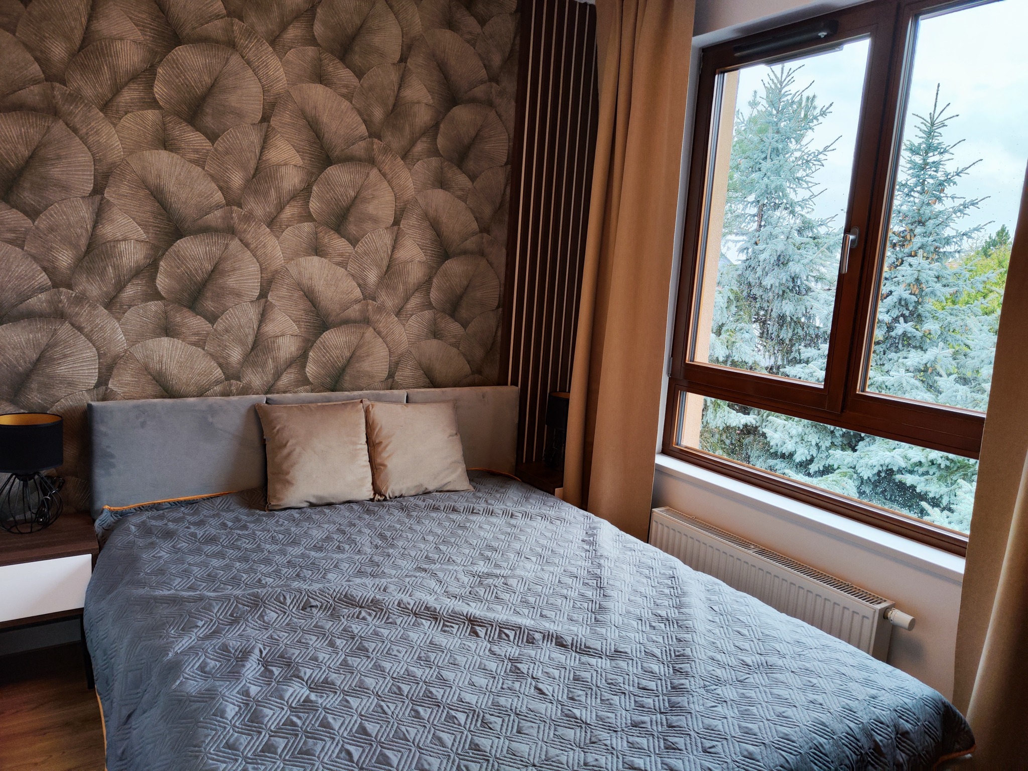 Sypialnia z łóżkiem, tapetą w liście i widokiem na zaśnieżone drzewa za oknem