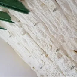 Nierówna warstwa białej pianki izolacyjnej, przytwierdzona metalowymi klamrami do zielonej konstrukcji nośnej, widoczne nieregularne struktury i pęcherzyki piany.