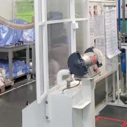 Mobilna stacja robocza z szlifierką polerską, wyposażona w przezroczystą osłonę i oświetlenie, umieszczona w hali produkcyjnej.
