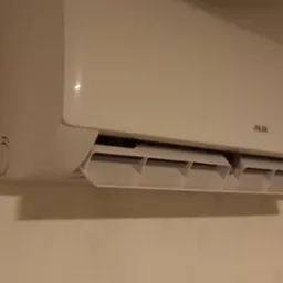 Biały klimatyzator marki AUX zamontowany na jasnej ścianie, z widocznym wyświetlaczem temperatury ustawionym na 22 stopnie Celsjusza.