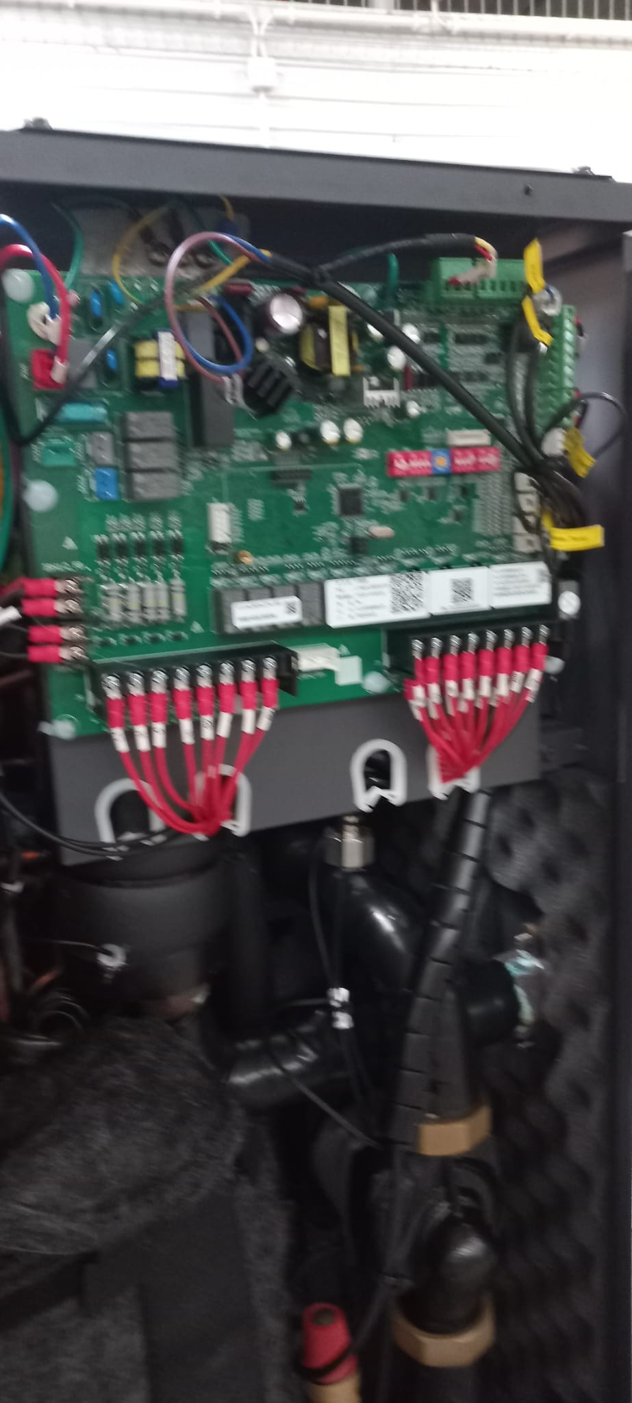 Wnętrze urządzenia z widoczną płytą sterującą, licznymi przewodami i elementami hydraulicznymi; ujęcie z bliska, widoczne detale połączeń.