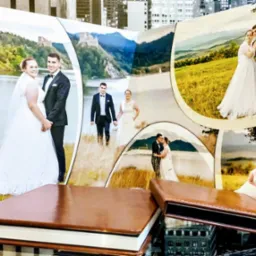 Otwarty album ślubny z kolażem zdjęć pary młodej na tle krajobrazów, leżący na szklanej powierzchni z odbiciem miejskiej panoramy.