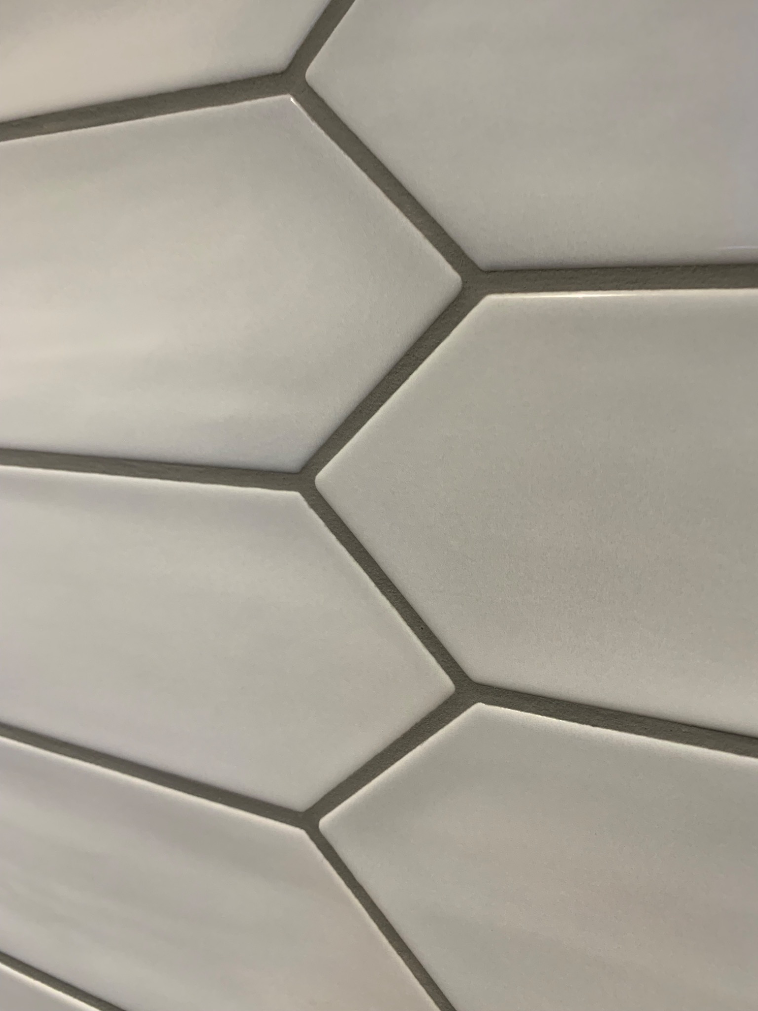 Detaliczne ujęcie białych, heksagonalnych płytek ceramicznych ułożonych z szarą fugą, sfotografowanych pod kątem.
