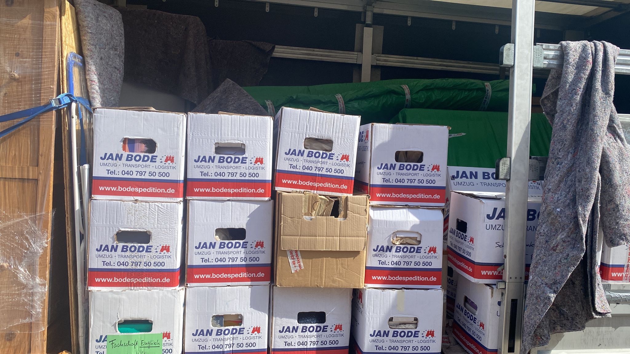 Wnętrze samochodu dostawczego załadowane kartonami z logo firmy przeprowadzkowej Jan Bode, zabezpieczone kocami i folią.