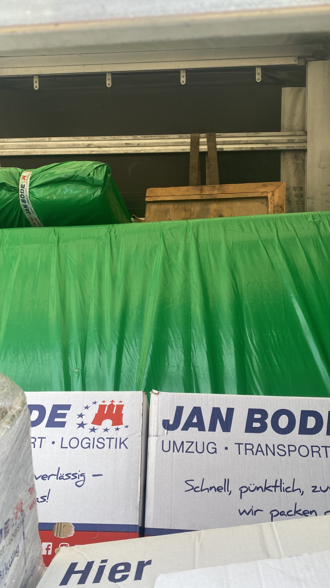 Wnętrze skrzyni ładunkowej wypełnione kartonami firmy Jan Bode, zabezpieczonymi zieloną folią, gotowymi do transportu.