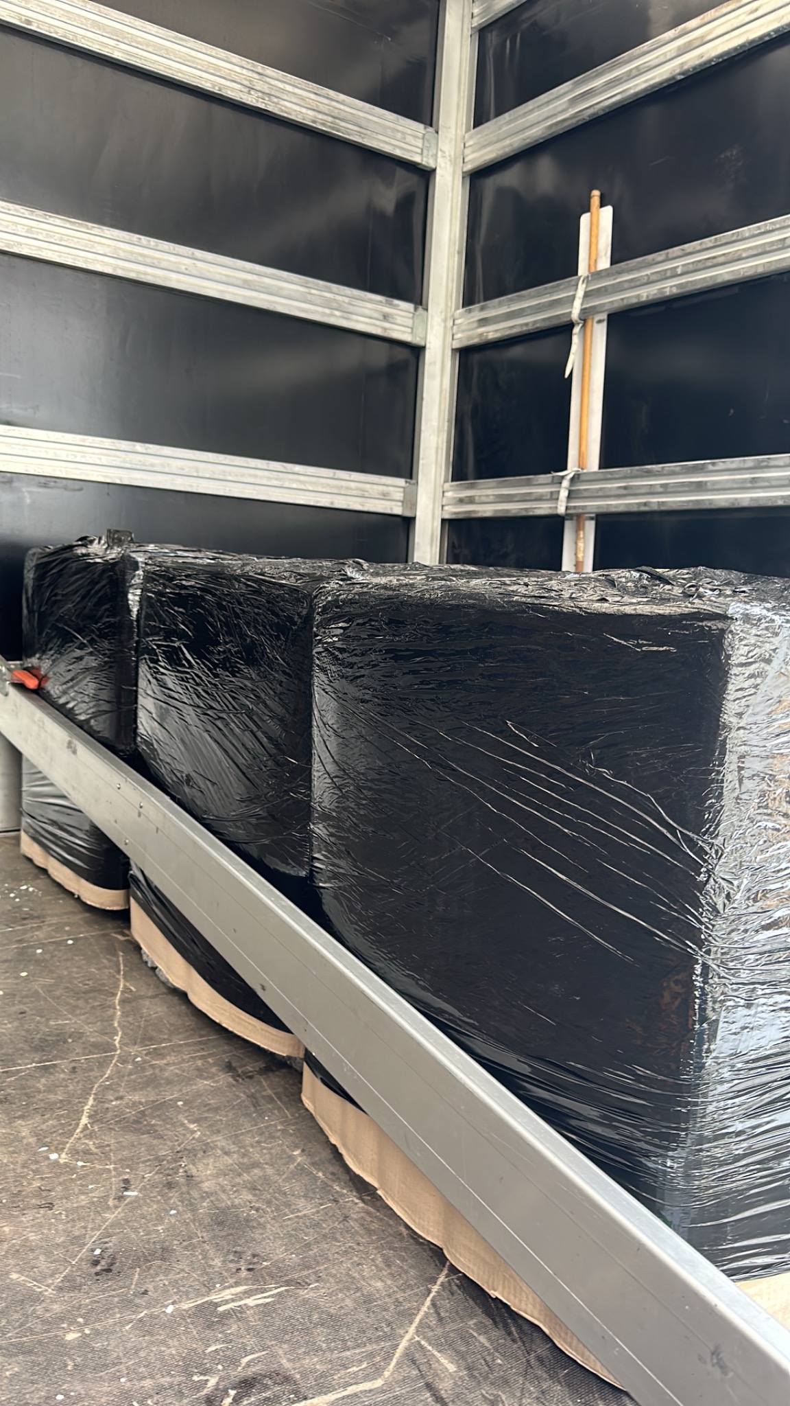 Czarne, owinięte folią ładunki zabezpieczone wewnątrz przestrzeni ładunkowej pojazdu z metalową konstrukcją.