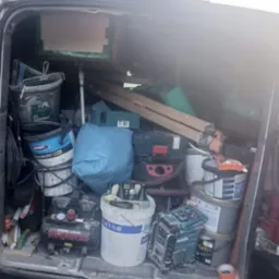 Wnętrze busa wypełnione wiadrami z farbą, narzędziami i sprzętem budowlanym, w tym kompresorem Pro-Line Herkules i radiem Makita, sugerujące przygotowania do prac wykończeniowych.