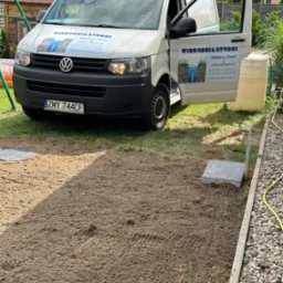 Wiercenie studni: Biały samochód dostawczy z otwartymi drzwiami i naklejką firmy w tle, świeżo nawiercona studnia z kranem i betonową podstawą na pierwszym planie.