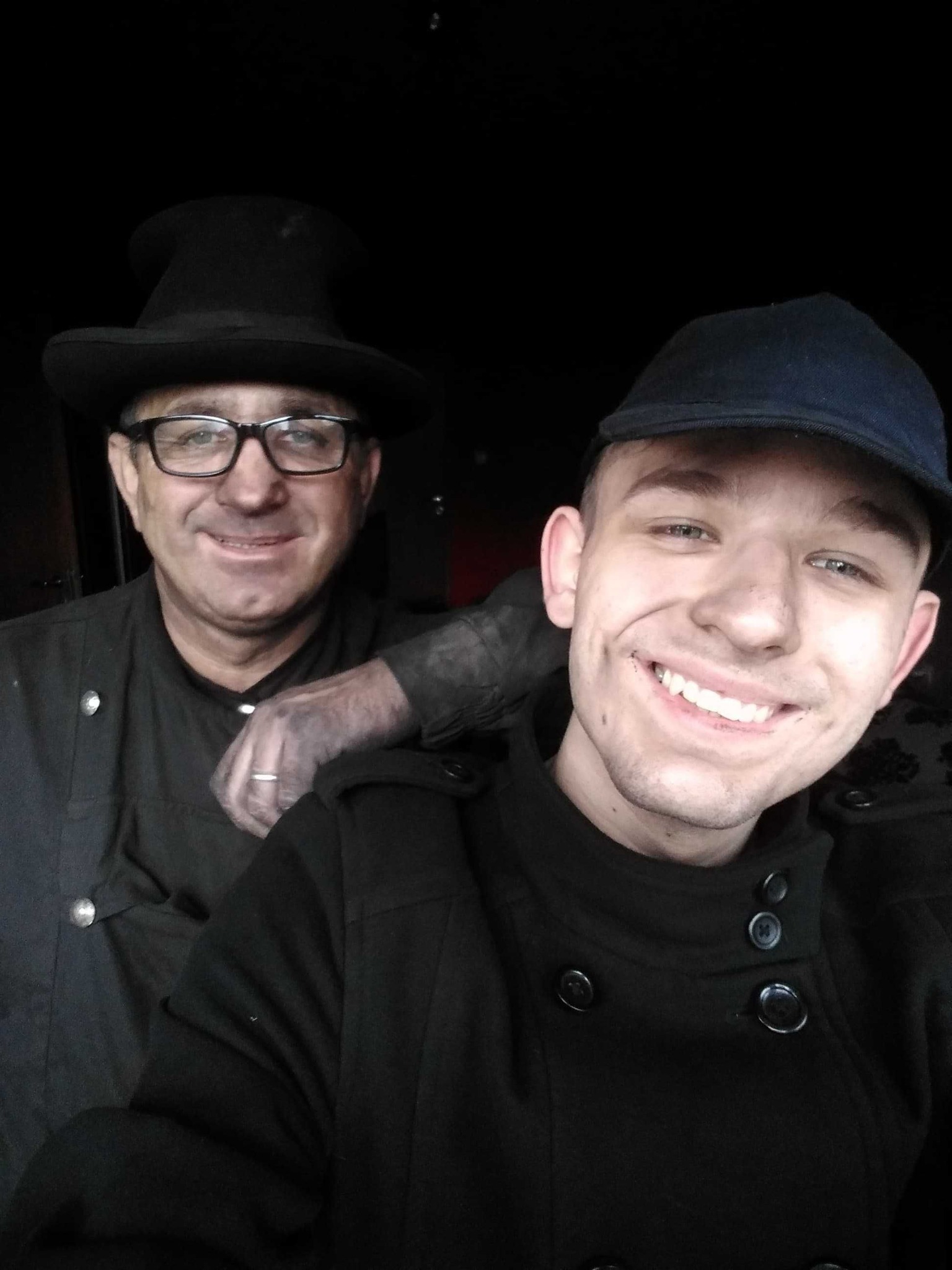 Portret dwóch uśmiechniętych mężczyzn w czarnych ubraniach roboczych, z których jeden ma zabrudzoną sadzą twarz, a drugi nosi cylinder i okulary, pozujących do zdjęcia.