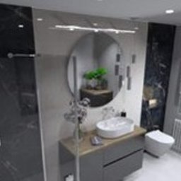 Zbigniew Banasiak - Wizualizacja nowoczesnej łazienki z czarno-białymi płytkami imitującymi marmur, okrągłym lustrem, minimalistyczną umywalką nablatową i grzejnikiem żeberkowym pod oknem z żaluzjami.