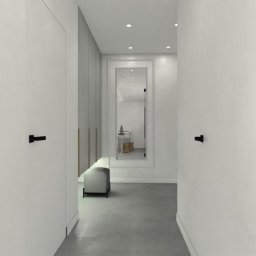 Zbigniew Banasiak - Minimalistyczny przedpokój w odcieniach bieli i szarości z czarnymi klamkami, lustrem w białej ramie i pufą.