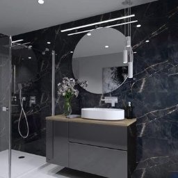 Zbigniew Banasiak - Nowoczesna łazienka z czarnymi marmurowymi płytkami, kabiną prysznicową typu walk-in, okrągłym lustrem i umywalką nablatową na szarej szafce.