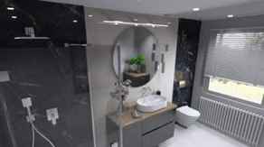 Wizualizacja nowoczesnej łazienki z czarno-białymi płytkami imitującymi marmur, okrągłym lustrem, minimalistyczną umywalką nablatową i grzejnikiem żeberkowym pod oknem z żaluzjami.