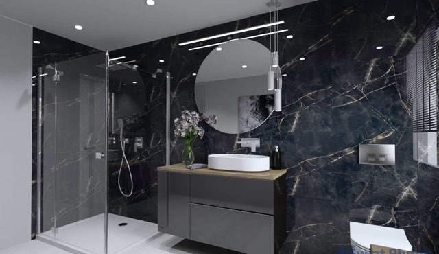 Nowoczesna łazienka z czarnymi marmurowymi płytkami, kabiną prysznicową typu walk-in, okrągłym lustrem i umywalką nablatową na szarej szafce.