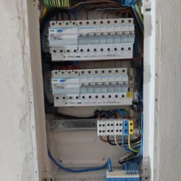 Rozdzielnica elektryczna Hager w trakcie montażu, widoczne zabezpieczenia nadprądowe, różnicowoprądowe, listwy zaciskowe w kolorach zielonym, niebieskim i żółto-niebieskim, przewody w różnych...