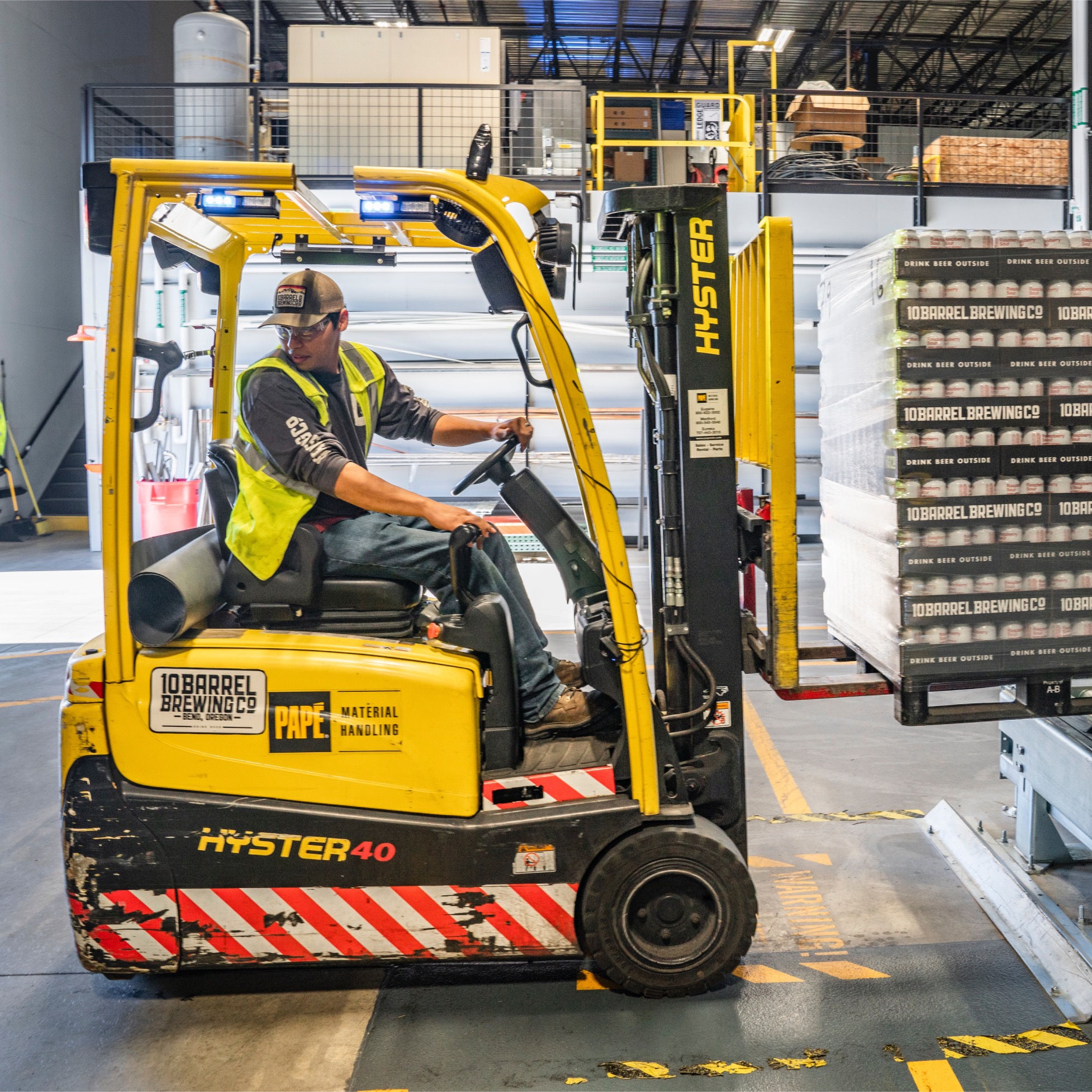 Operator w wózku widłowym Hyster 40 transportuje paletę z napojami 10 Barrel Brewing Co. w hali magazynowej w Gdańsku. W tle widoczne regały i elementy infrastruktury magazynowej.